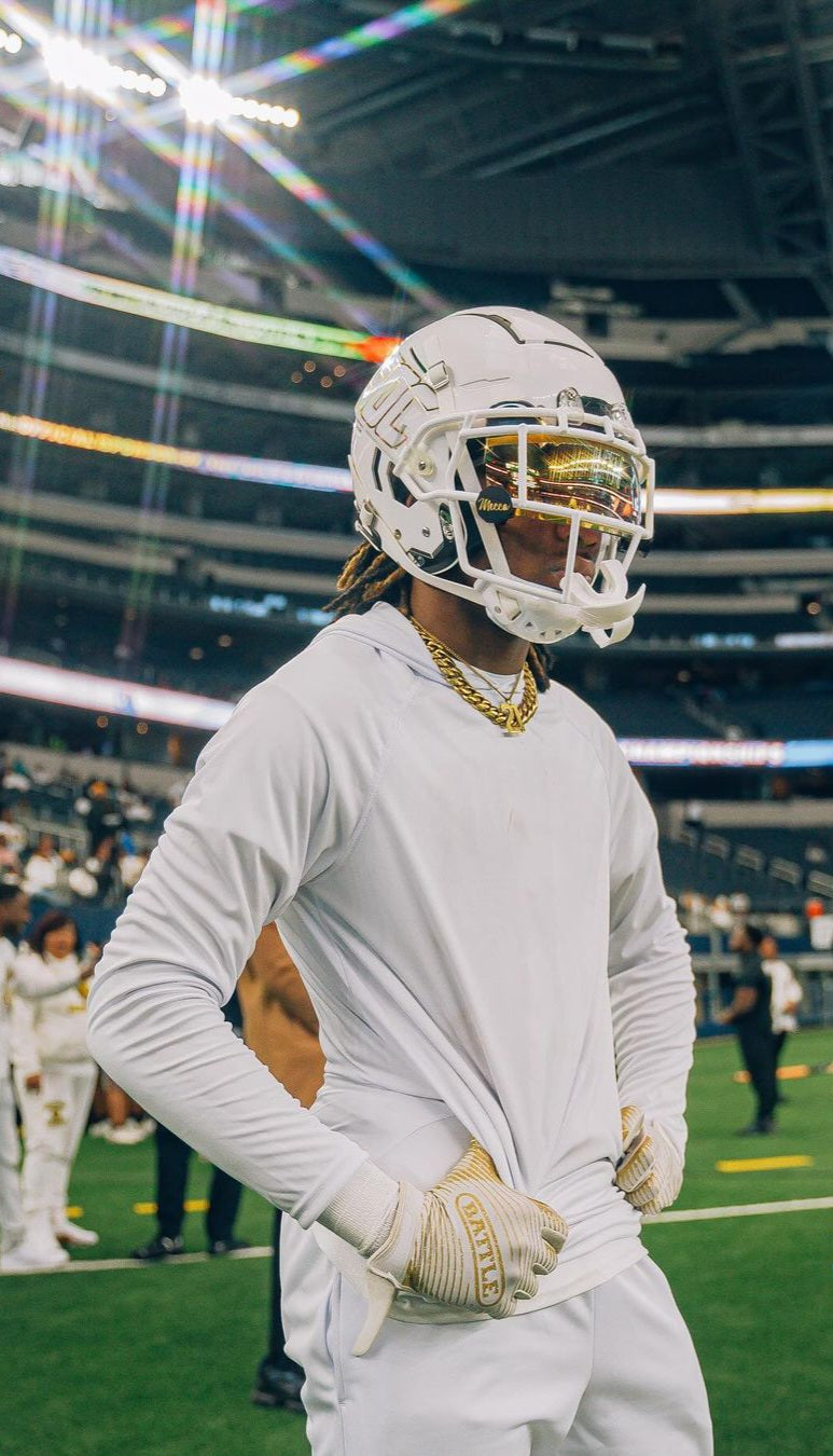 Player wearing all white with white football helmet, with gold visor and black visor clips that read mecca in gold writing.